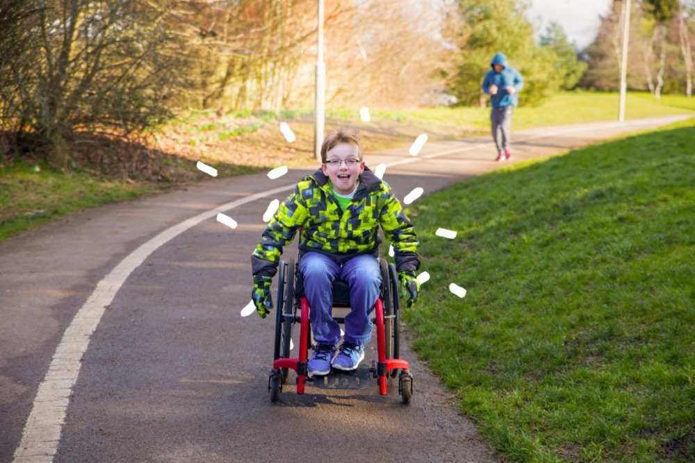 A young wheelchair user wheels down a park pathway