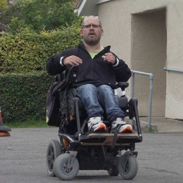 Our wheelchair skills trainer in his powered chair outside a single story building