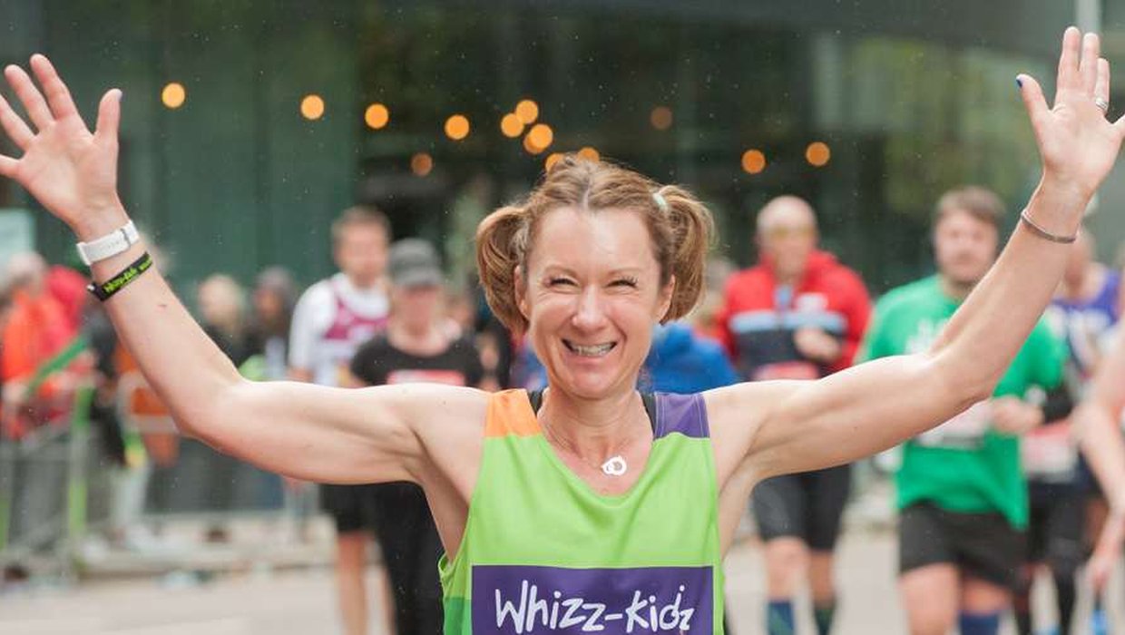 A runner in a green Whizz Kidz top waves with both hands
