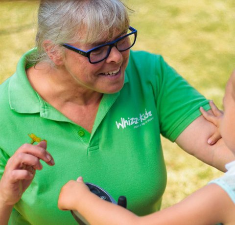 A Whizz Kidz staff member smiles with a young wheelchair user