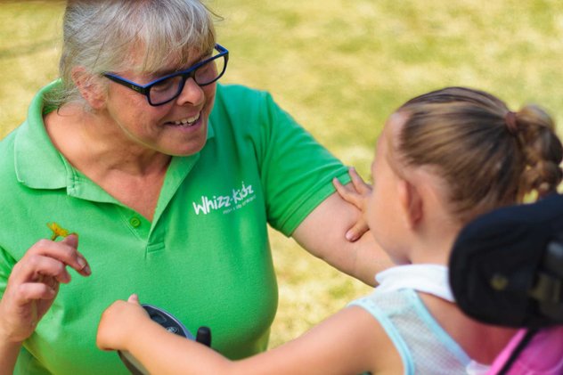 A Whizz Kidz staff member smiles with a young wheelchair user