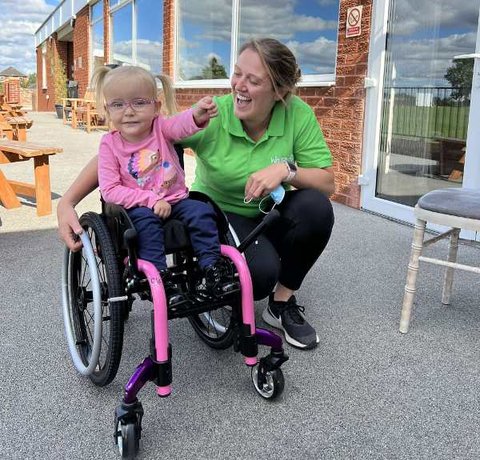 Luna in her awesome pink wheelchair with a Whizz Kidz team member next to her