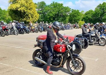 A number of motorcycles with their riders in a car park on a sunny day