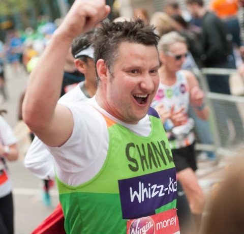 A runner in a green Whizz Kidz top raised his arm as he runs past the camera