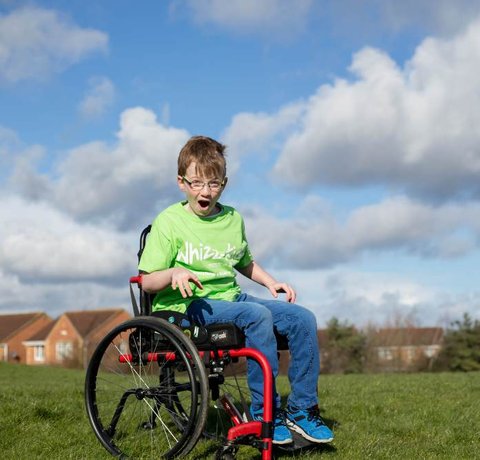 McKenzie wears a green Whizz-Kidz T-shirt in a manual wheelchair in an open field