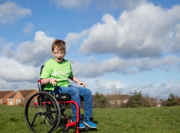 McKenzie wears a green Whizz-Kidz T-shirt in a manual wheelchair in an open field