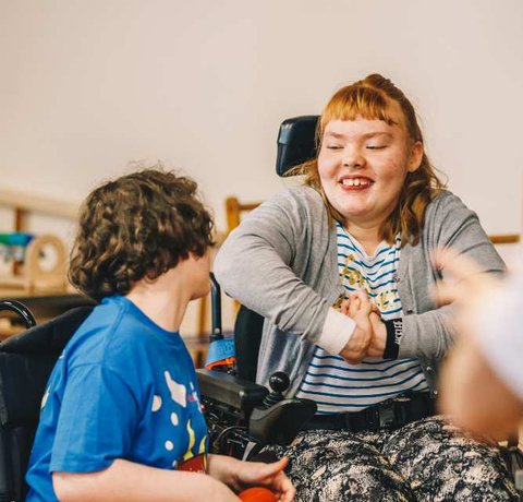 Two young wheelchair users smile at each other