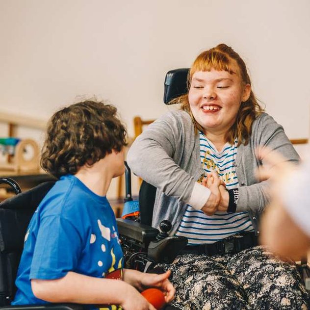 Two young wheelchair users smile at each other