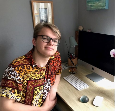 A young adult sits at a neat desk with a computer in front of him