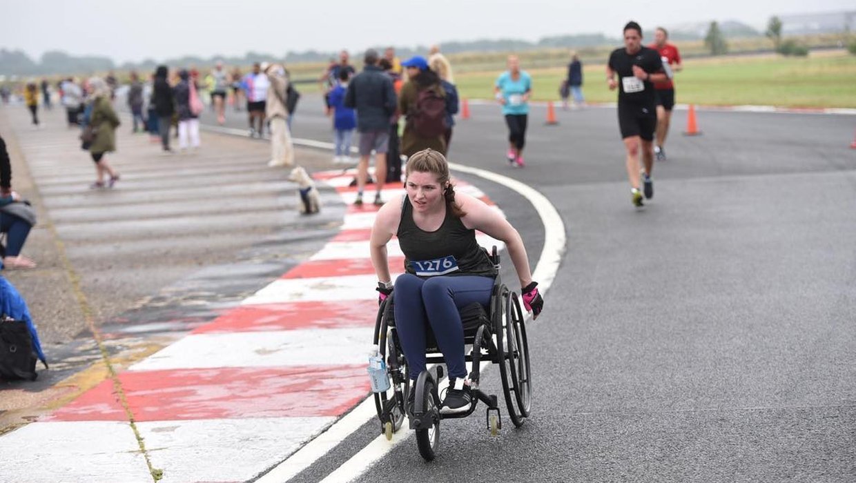 Ella in a racing wheelchair going around a track, training for the marathon.