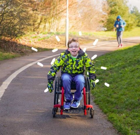 A young wheelchair user wheels down a park pathway