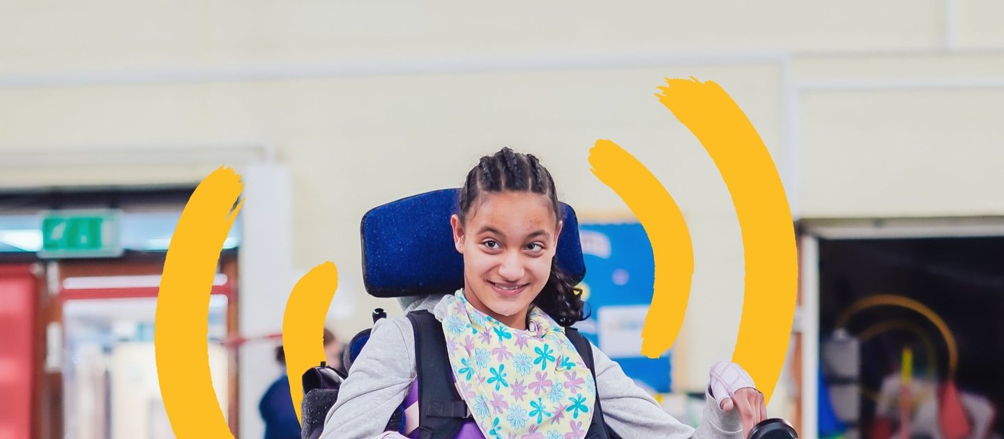 A young wheelchair user is smiling, using her powered wheelchair in a sports hall