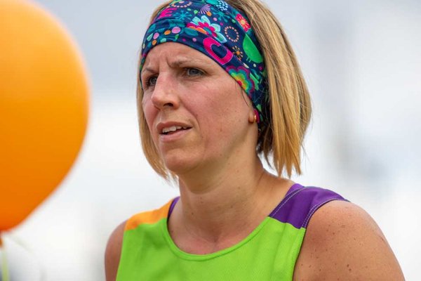 Close up on a runner's face, wearing a green Whizz Kidz running top and a multi-coloured head band