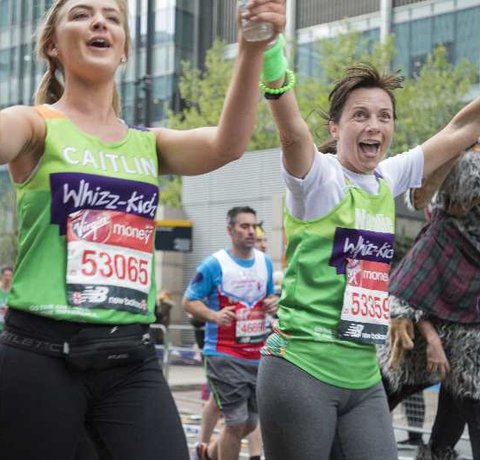 Two Whizz Kidz marathon runners, hold their hands up whilst looking incredibly stylish in their Whizz Kidz vests