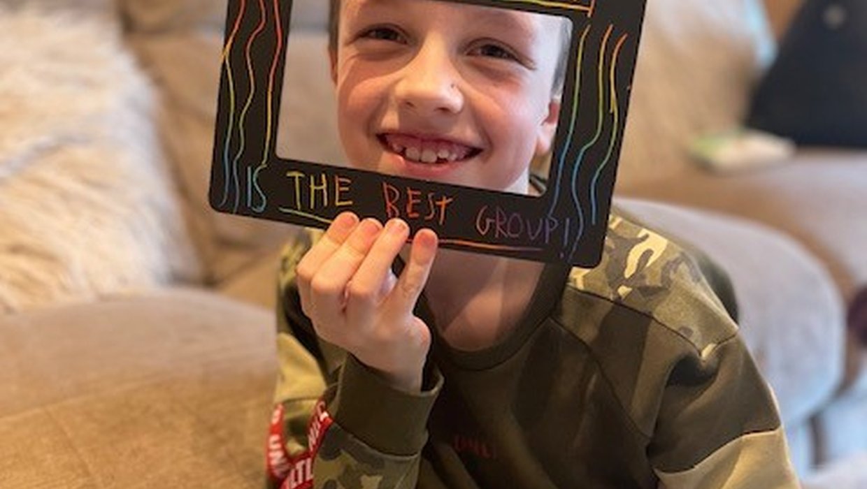 A child holds a frame in front of him that reads 'Sibling Group the best group'