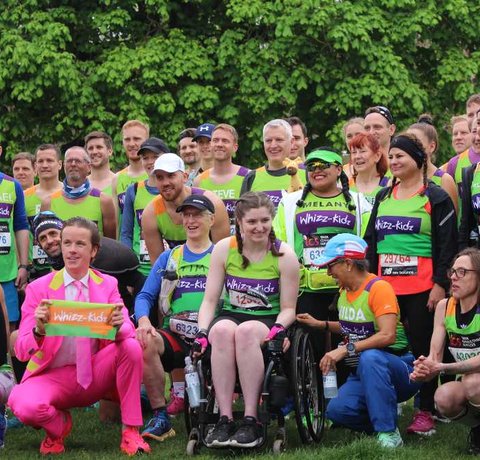 A large group of runners in the Whizz Kidz green vest posing for a group photo