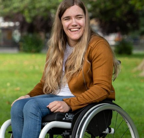 A young wheelchair user sits smiling in a park