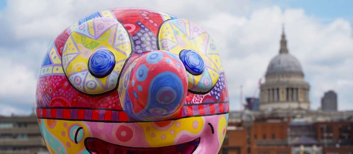 Jason Wilsher-Mill's Morph's head in close up. He is in front of the river Thames, with London skyline behind him. Morph's head features an intricate psychedelic pattern, including stars on his eyes and a union flag mask.